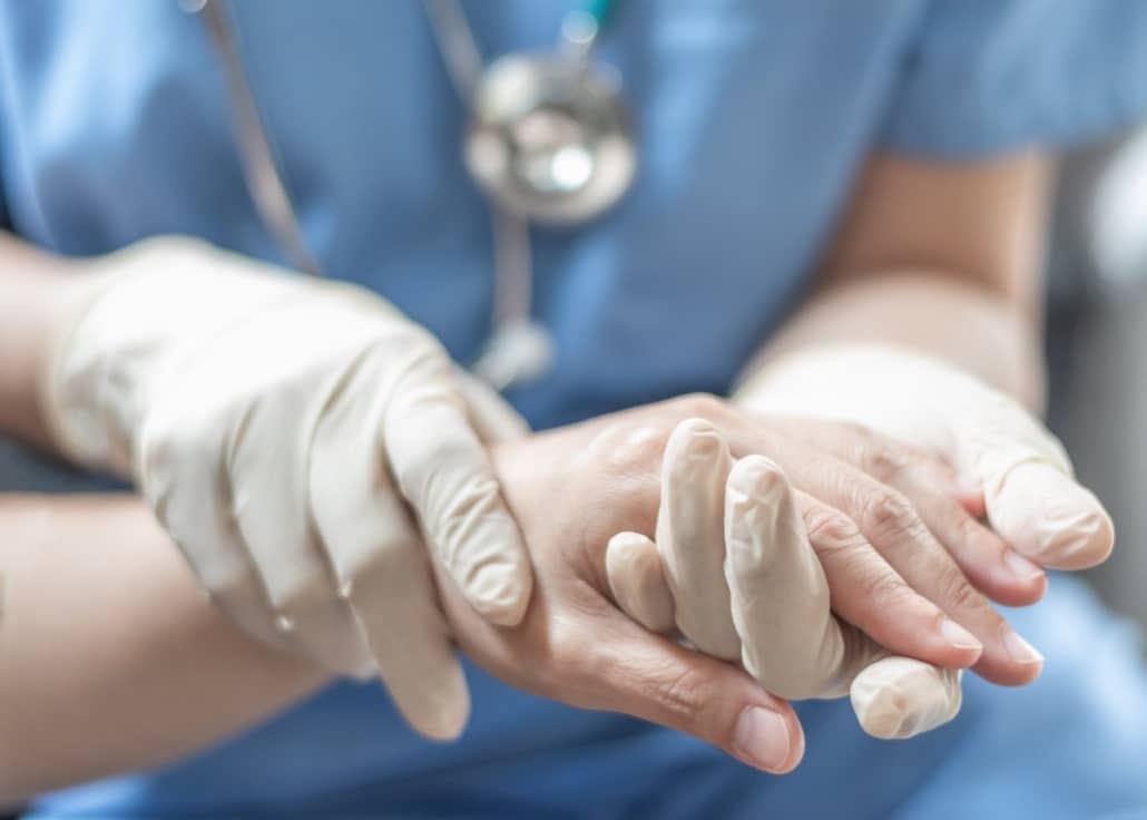 A doctor in gloves holding a patient’s hand