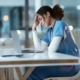 A stressed-out nurse sits in front of a laptop with her head in her hands