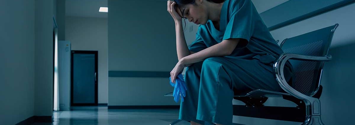 A burned-out nurse sits in a waiting room chair with her head in her hands