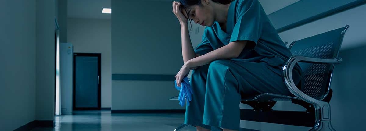 A burned-out nurse sits in a waiting room chair with her head in her hands