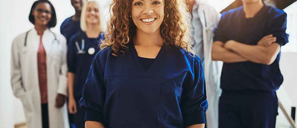 A smiling healthcare worker stands with a team of hospital staff