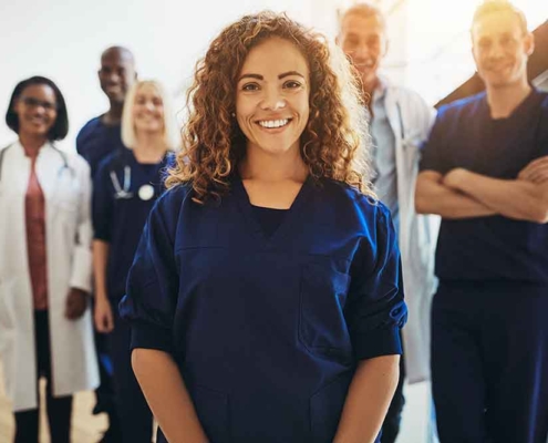A smiling healthcare worker stands with a team of hospital staff